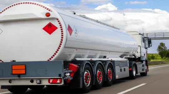 Citerne de stockage propane professionnelle aérienne blanche installée sur dalle béton avec garde-corps et marquages GPL réglementaires, sur site d'établissement saisonnier français avec végétation locale en arrière-plan