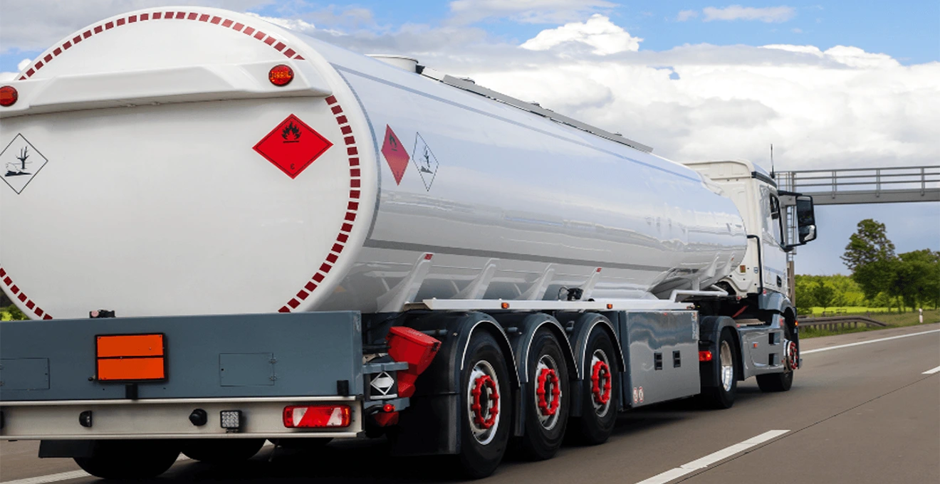 Citerne de stockage propane professionnelle aérienne blanche installée sur dalle béton avec garde-corps et marquages GPL réglementaires, sur site d'établissement saisonnier français avec végétation locale en arrière-plan